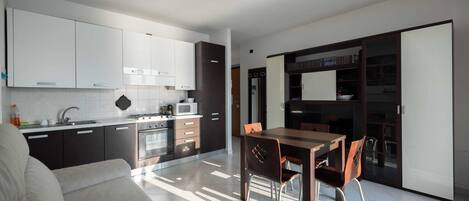 Une cuisine moderne avec des meubles blancs, un coin repas avec une table et des chaises en bois, et une porte-fenêtre coulissante donnant sur un espace de vie.