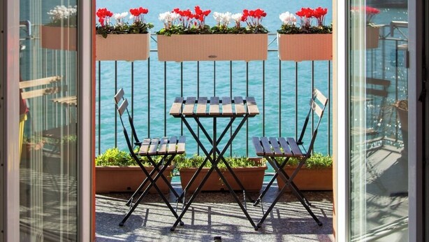 Un balcon avec une table et des chaises, donnant sur un lac avec des montagnes en arrière-plan.