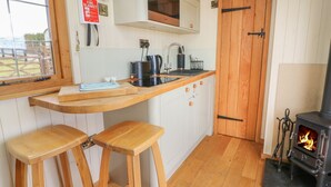A kitchen with wooden stools, a microwave, a stove, and a fire blanket sign.
