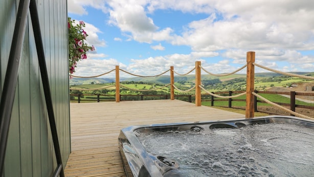 A wooden deck with a hot tub, surrounded by a rope barrier and wooden posts, overlooking a scenic landscape.
