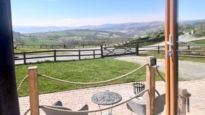 A scenic view from a balcony with a rope barrier, a table, and chairs. - Highland View -  a shepherds hut that sleeps 2 guests  in 1 bedroom (Rhayader)