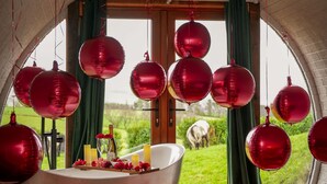 A room with a large bathtub, red spherical decorations, and a view of greenery outside. - Hedgehogs View -  a hobbit hut that sleeps 6 guests  in 3 bedrooms (Rhayader)