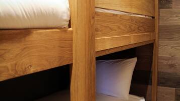 Uma cama de beliche com estruturas de madeira e roupa de cama branca, diante de uma parede de tijolos e soalho de madeira.