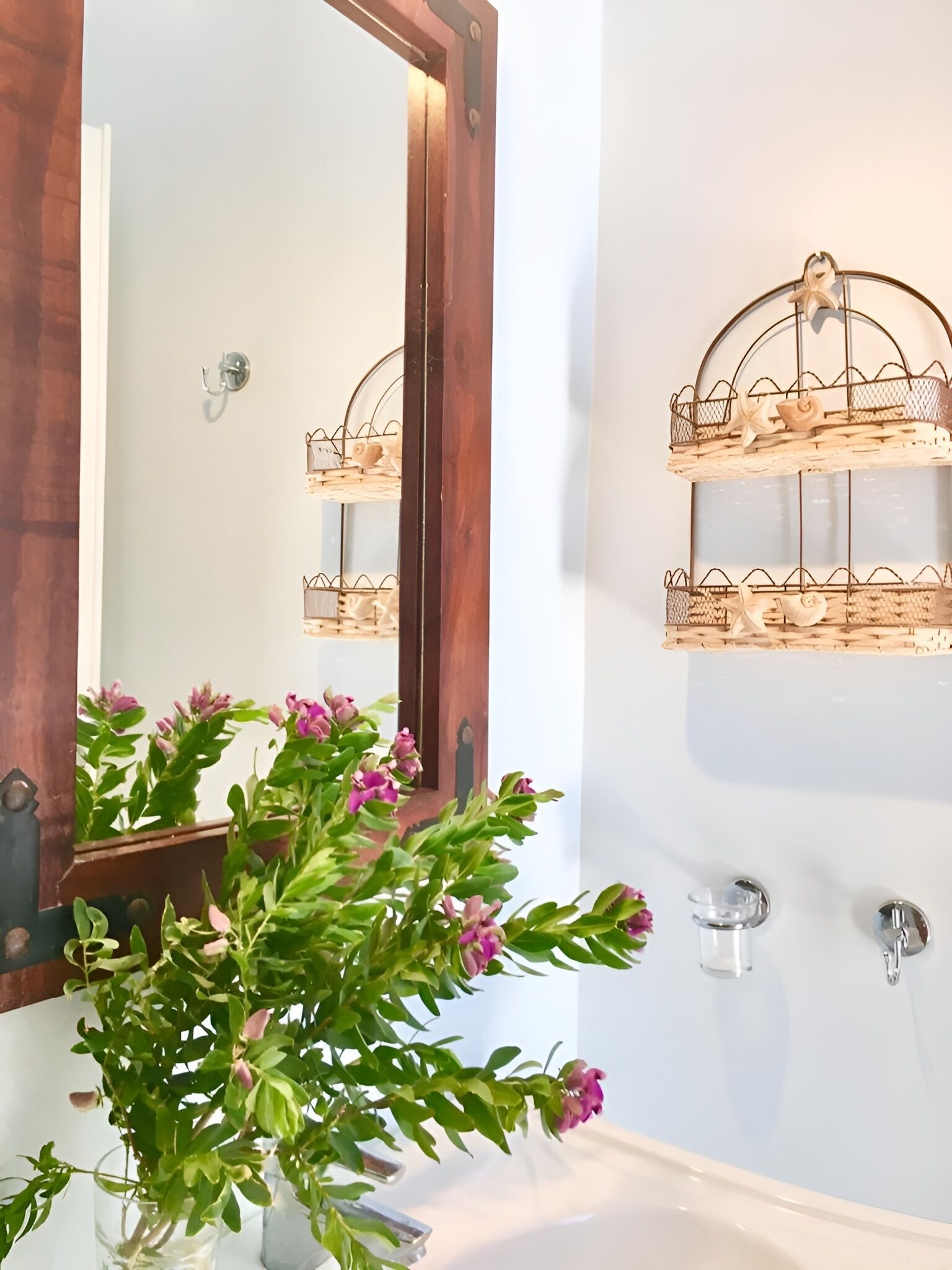 A bathroom with a large mirror, a wooden door, a white sink, and a wall-mounted shelf with decorative items.