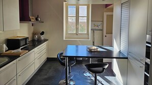 A compact kitchen with a dining area, a window, and a door leading to another room.