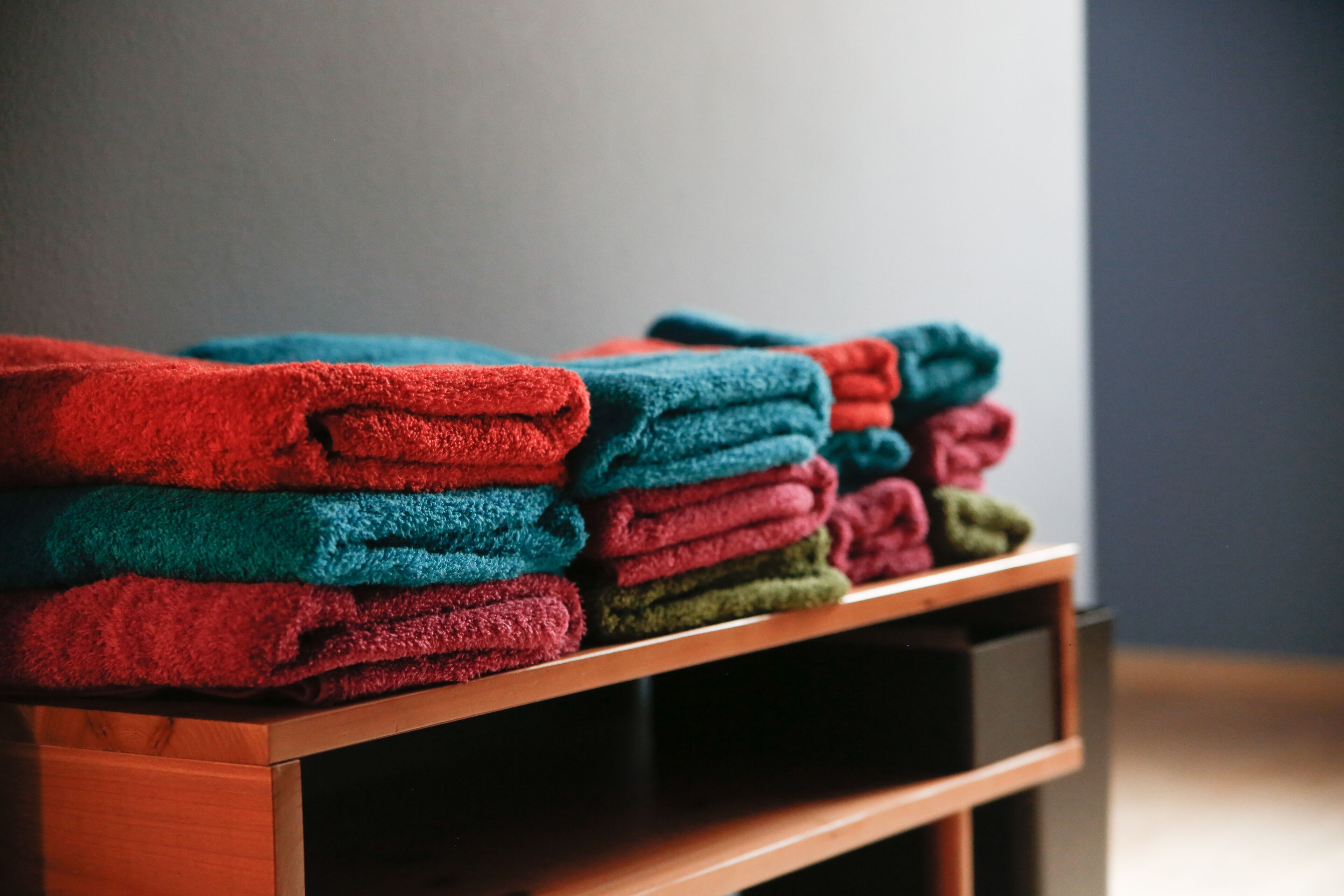 A stack of folded towels in various colors on a wooden shelf.