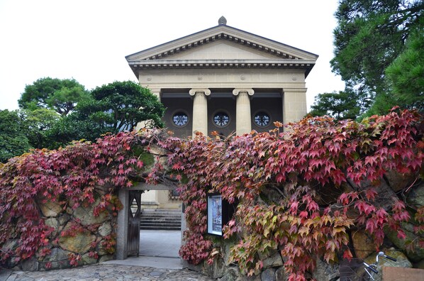 A classical building with columns and a pediment, surrounded by ivy-covered walls. - kurashinoyado temari madoromi (Kurashiki)