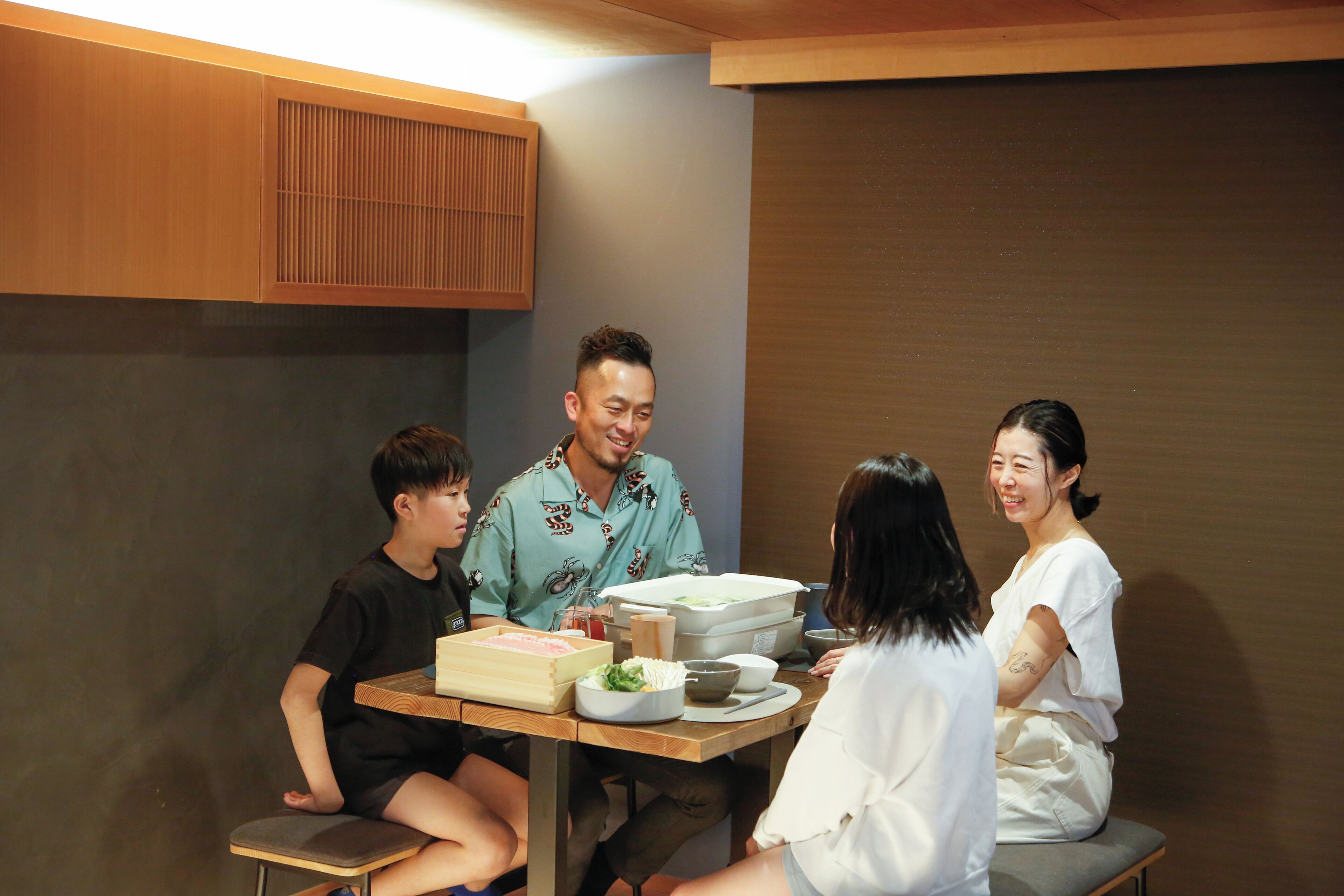 A group of people seated around a table with food and drinks, in a room with wooden paneling and a low ceiling.