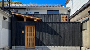 A modern building with a dark textured wall, a wooden door, and a small staircase leading to a covered area.