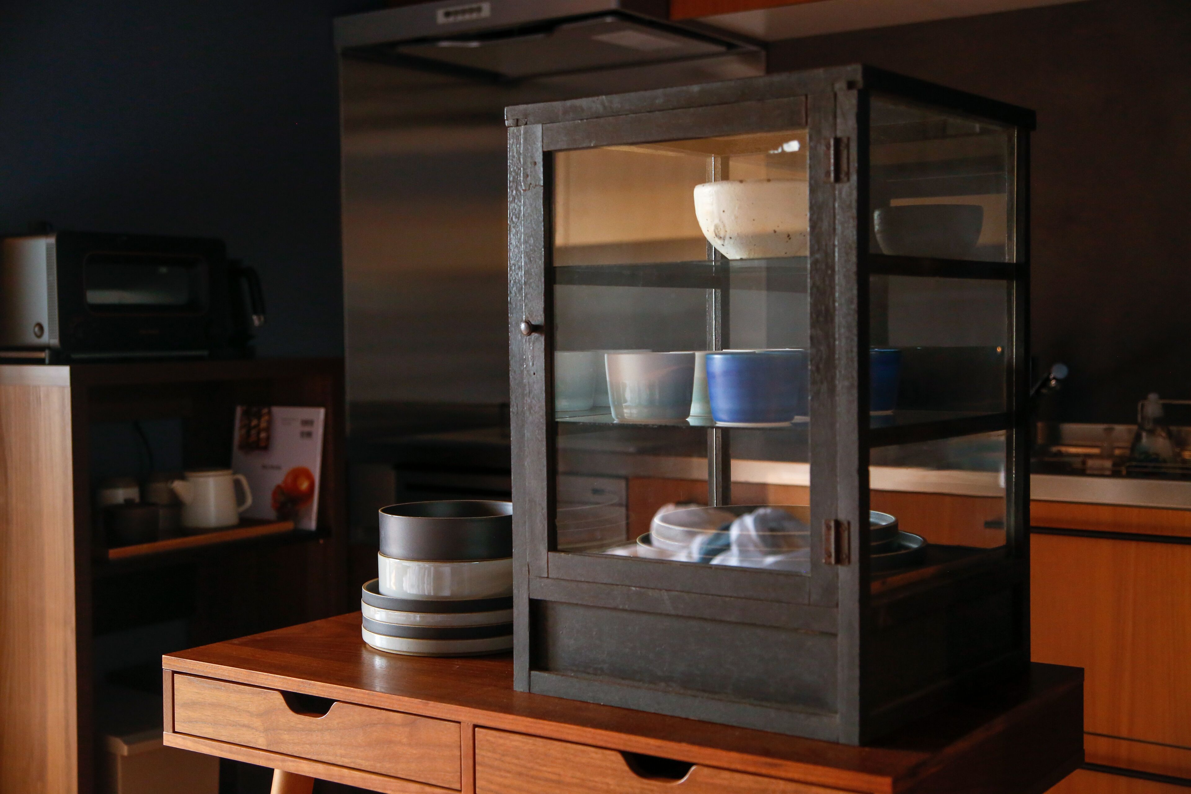 A kitchen with a microwave, a wooden table, and a glass-fronted cabinet with dishes.