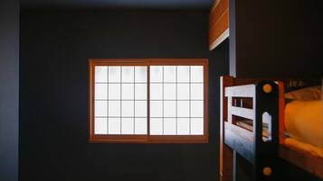 A room with a bunk bed, a window with a grid pattern, and a dark wall.