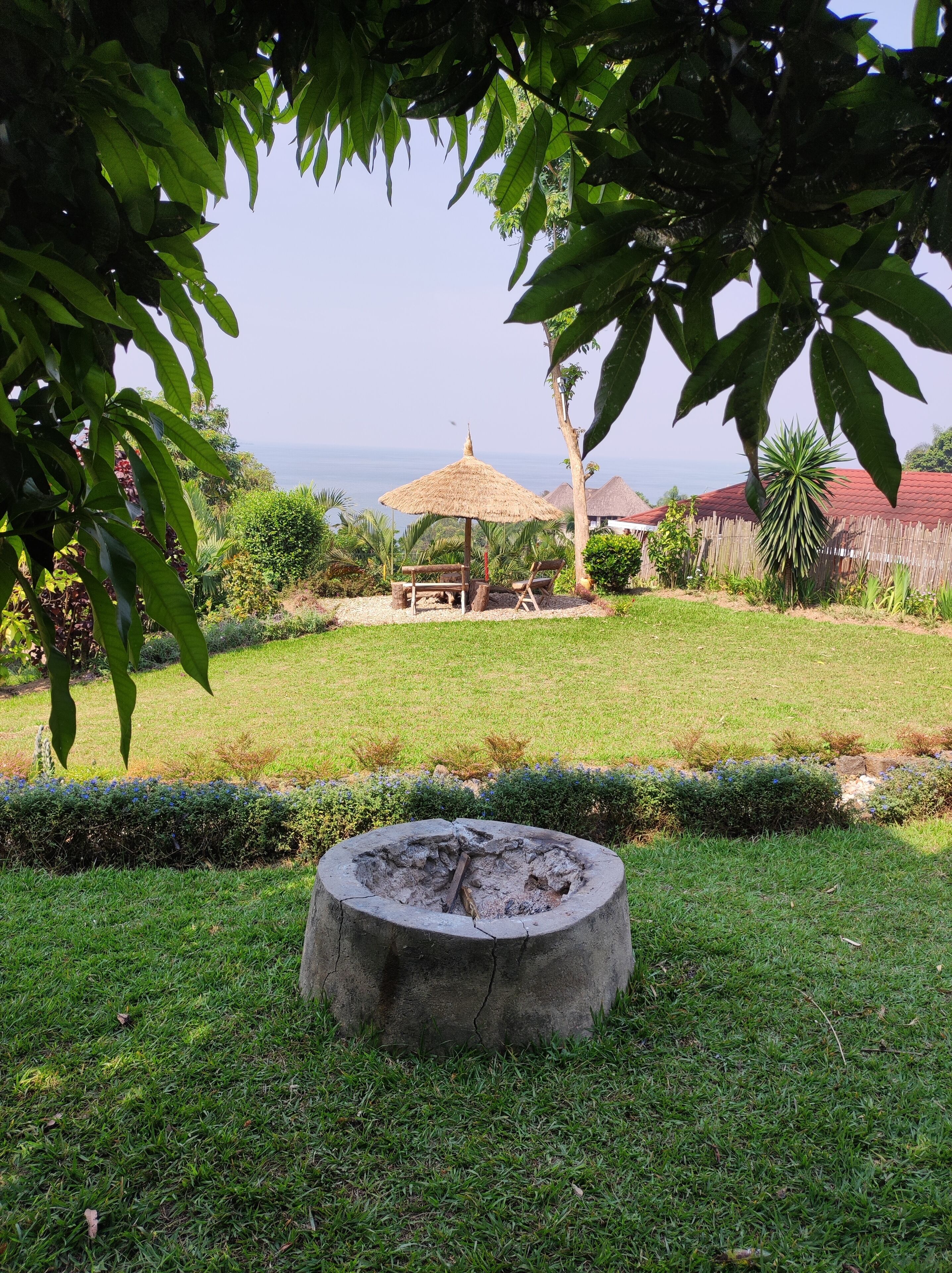 A garden with a fire pit, a wooden bench, and a thatched umbrella.
