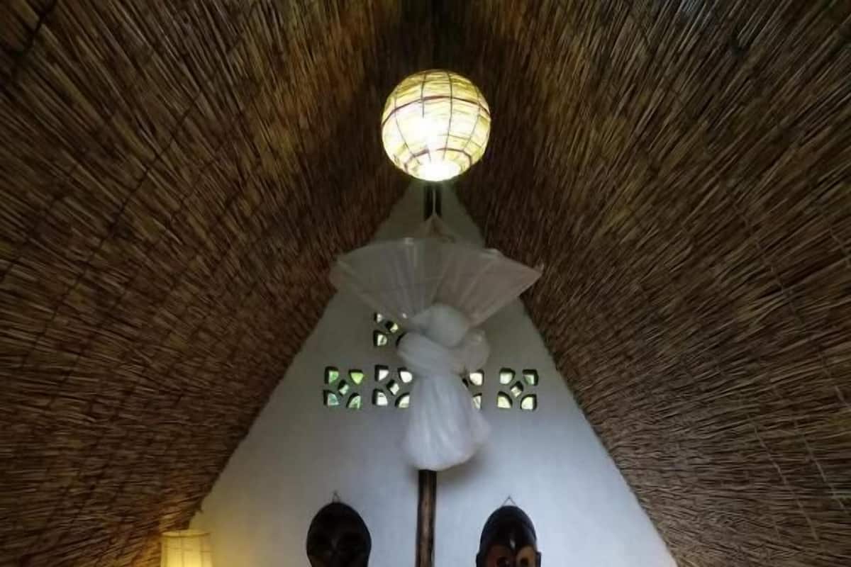 A room with a thatched roof, a bed with white bedding, a hanging light fixture, and two wall-mounted decorative items.