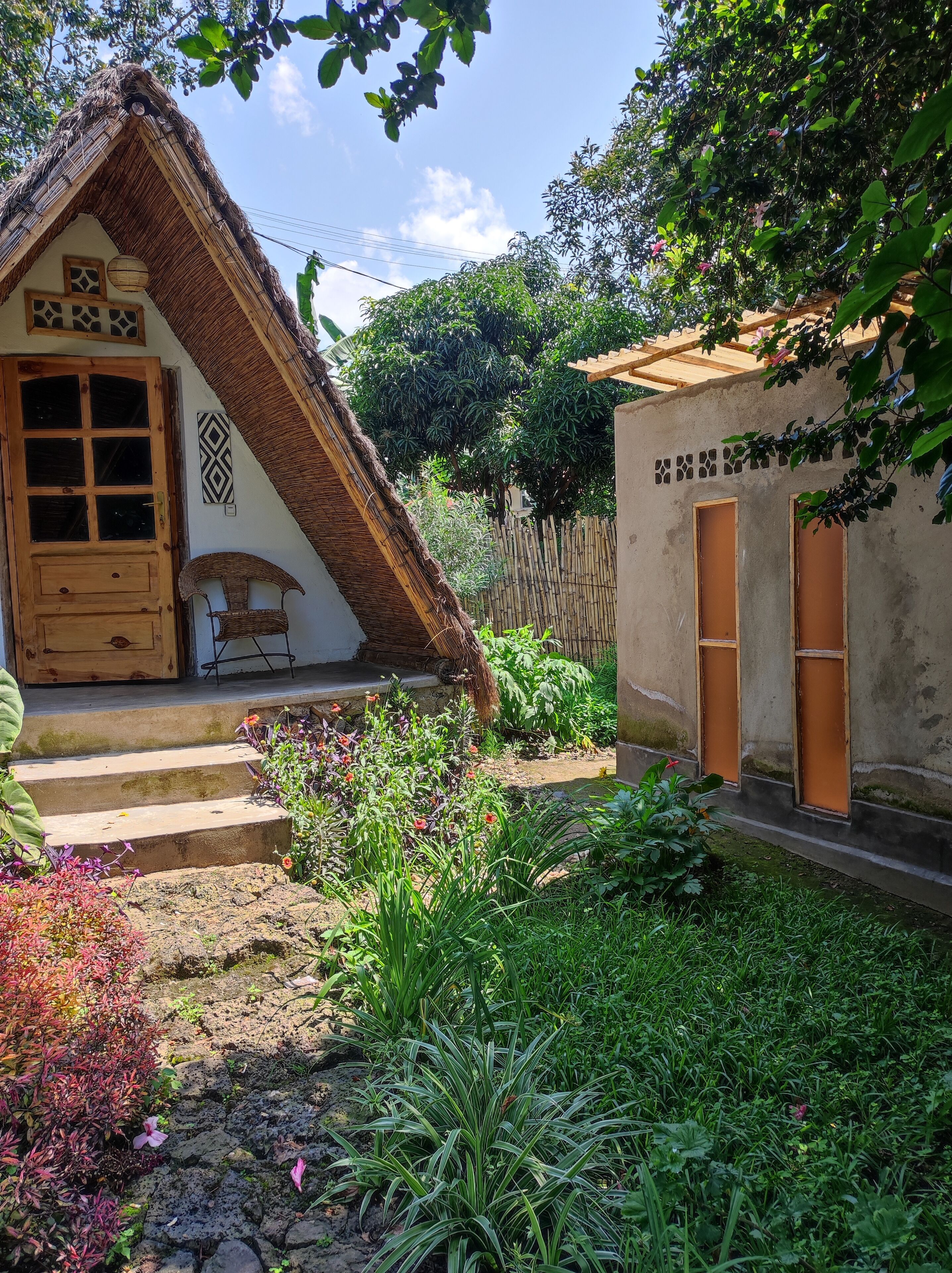 Una casa tradicional con techo de paja, puerta y ventanas de madera, rodeada por un jardín con diversas plantas y flores.