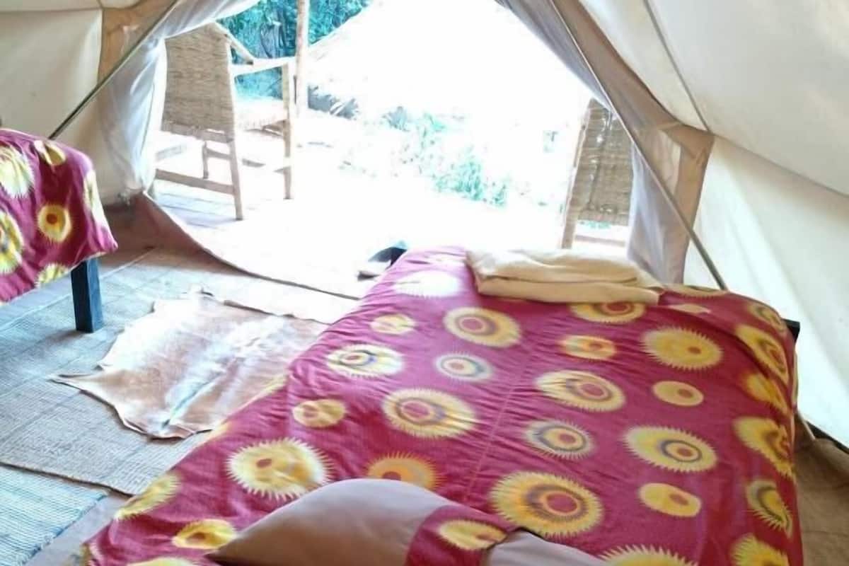 A tent with a bed featuring a sun pattern, a pillow, and a chair visible outside.