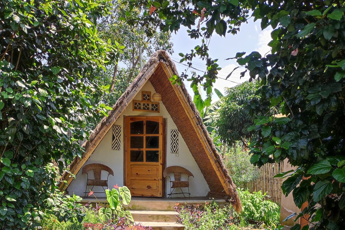 A thatched-roof cottage with a wooden door, surrounded by lush greenery and a garden path.