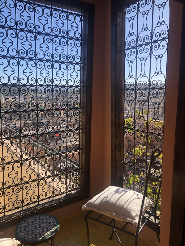 A balcony with ornate metal railings, a small round table, and a cushioned bench.