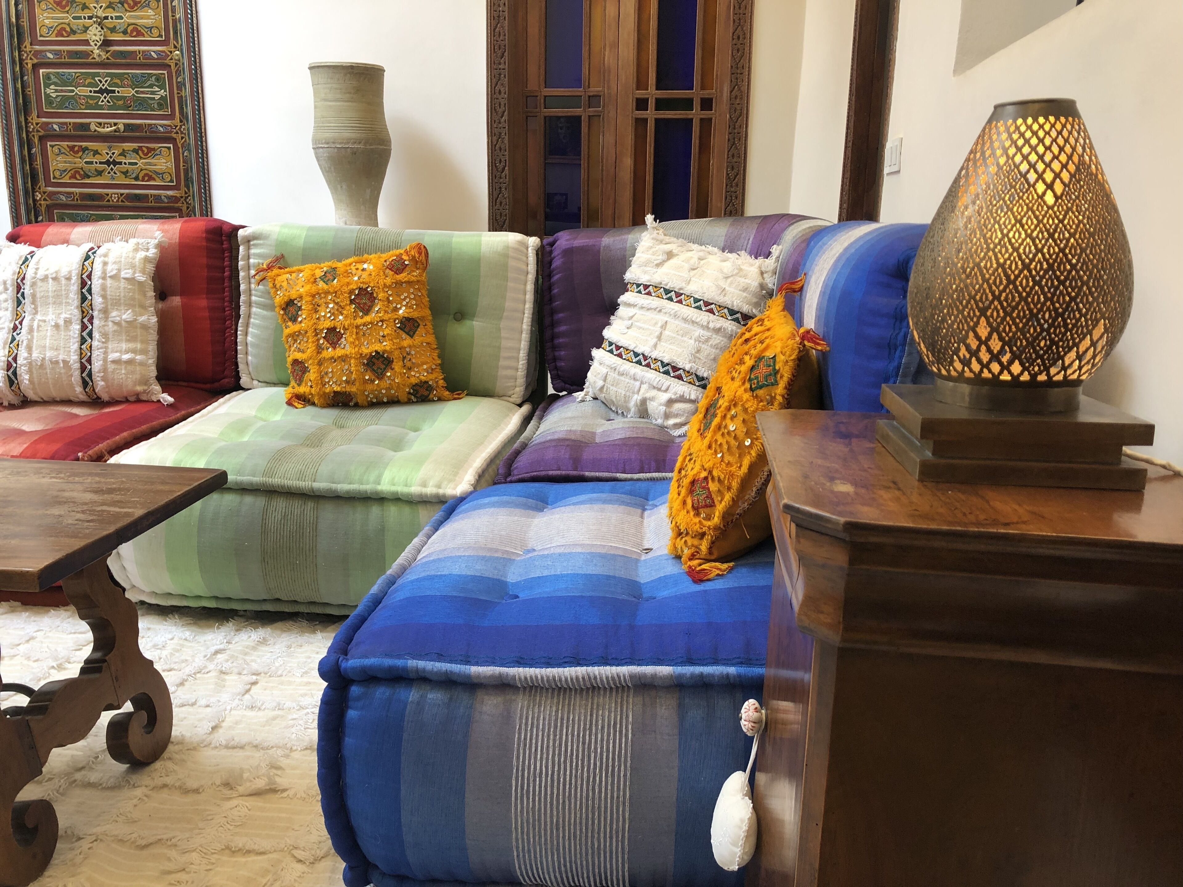Uma sala de estar acolhedora, com um sofá decorado com almofadas coloridas, um abajur e uma mesa de madeira.