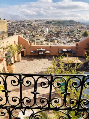 A rooftop terrace with outdoor seating, potted plants, and a view of a densely packed cityscape.