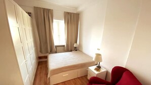 Ein Schlafzimmer mit einem Bett, einem Nachttisch, einem roten Sessel und einem Kleiderschrank.
