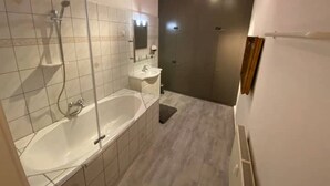 Ein modernes Badezimmer mit einer großen Badewanne, einer separaten Duschkabine und einem Waschtisch mit Spiegel.