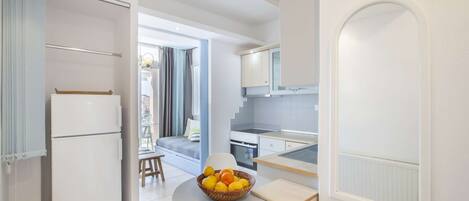 A compact kitchen with a dining area, a refrigerator, and a table with a fruit bowl.