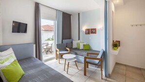 Un salon moderne comprenant un canapé, deux fauteuils, une petite table et un téléviseur fixé au mur.