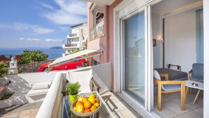 Un balcon avec une table, des chaises, un panier de fruits et une vue sur la mer.