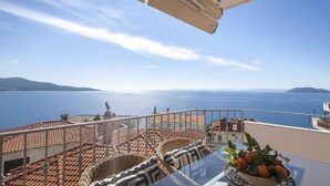 A terrace with a view of the sea, a table with a fruit bowl, and a wicker chair.