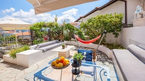 Une terrasse extérieure avec une table, des coussins, un hamac et un saladier rempli de fruits.