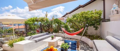 Een terras buiten met een tafel, kussens, een hangmat en een schaal fruit.