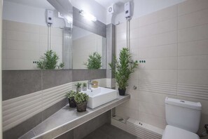 A bathroom with a white sink, mirror, and toilet. There are two potted plants on the counter and a towel rack above the sink.