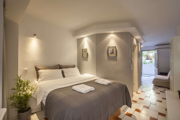 A modern hotel room with a large bed, a potted plant, and a view of the outdoor area.