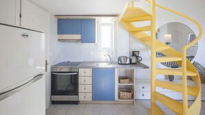 Eine kompakte Küche mit Einbauofen, Spüle und einer gelben Wendeltreppe.