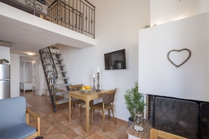A spacious living area with a dining table, chairs, a sofa, a fireplace, a TV, and a staircase leading to an upper level.