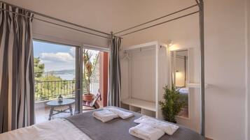 Une chambre d’hôtel avec un lit, un balcon doté d’une table et de chaises, un porte-manteau et une plante en pot.