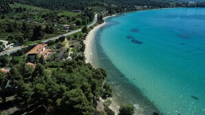 Vue aérienne d’une zone côtière avec une plage dégagée, une forêt dense et une route qui longe le rivage.