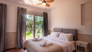 Une chambre à coucher avec un lit, une table de chevet, un ventilateur de plafond et une vue sur l’extérieur.