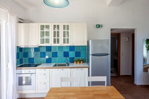 A modern kitchen with white cabinets, a blue-tiled backsplash, a stainless steel refrigerator, and a wooden dining table.