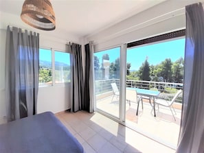 Quarto moderno com uma grande porta de vidro deslizante que dá para uma varanda com mesa e cadeiras.