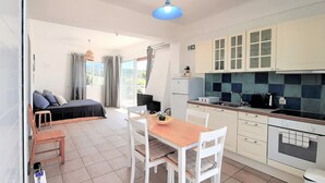 Una stanza compatta e luminosa, con un letto, un tavolo da pranzo con sedie, un angolo cottura con mobili ed elettrodomestici e vista da una finestra.