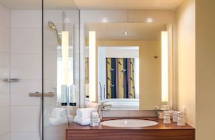 Un bagno moderno con box doccia in vetro, un mobile bagno in legno con lavandino tondo e uno specchio grande.