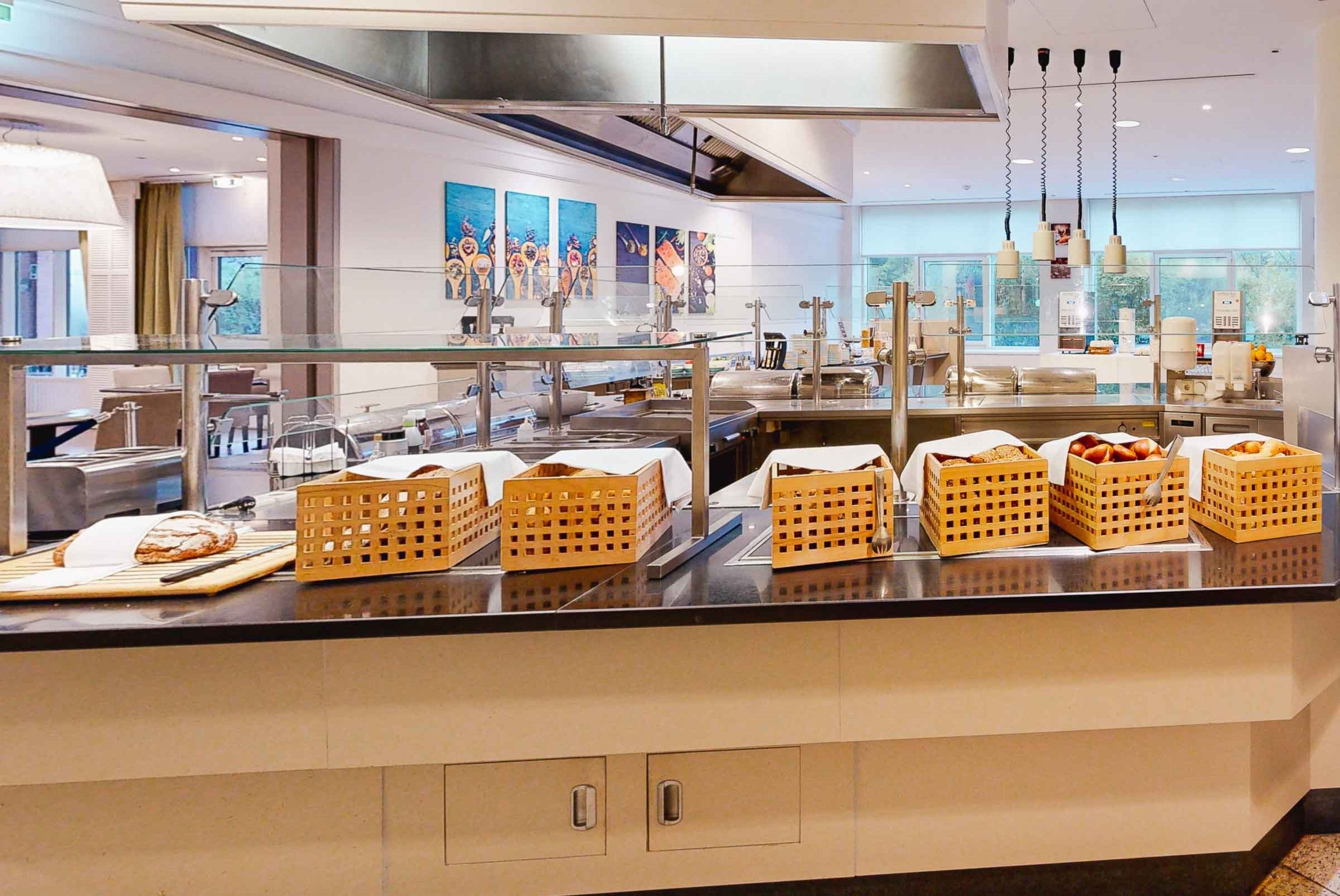 A modern breakfast bar with baskets of bread and pastries, stainless steel appliances, and artwork on the walls.