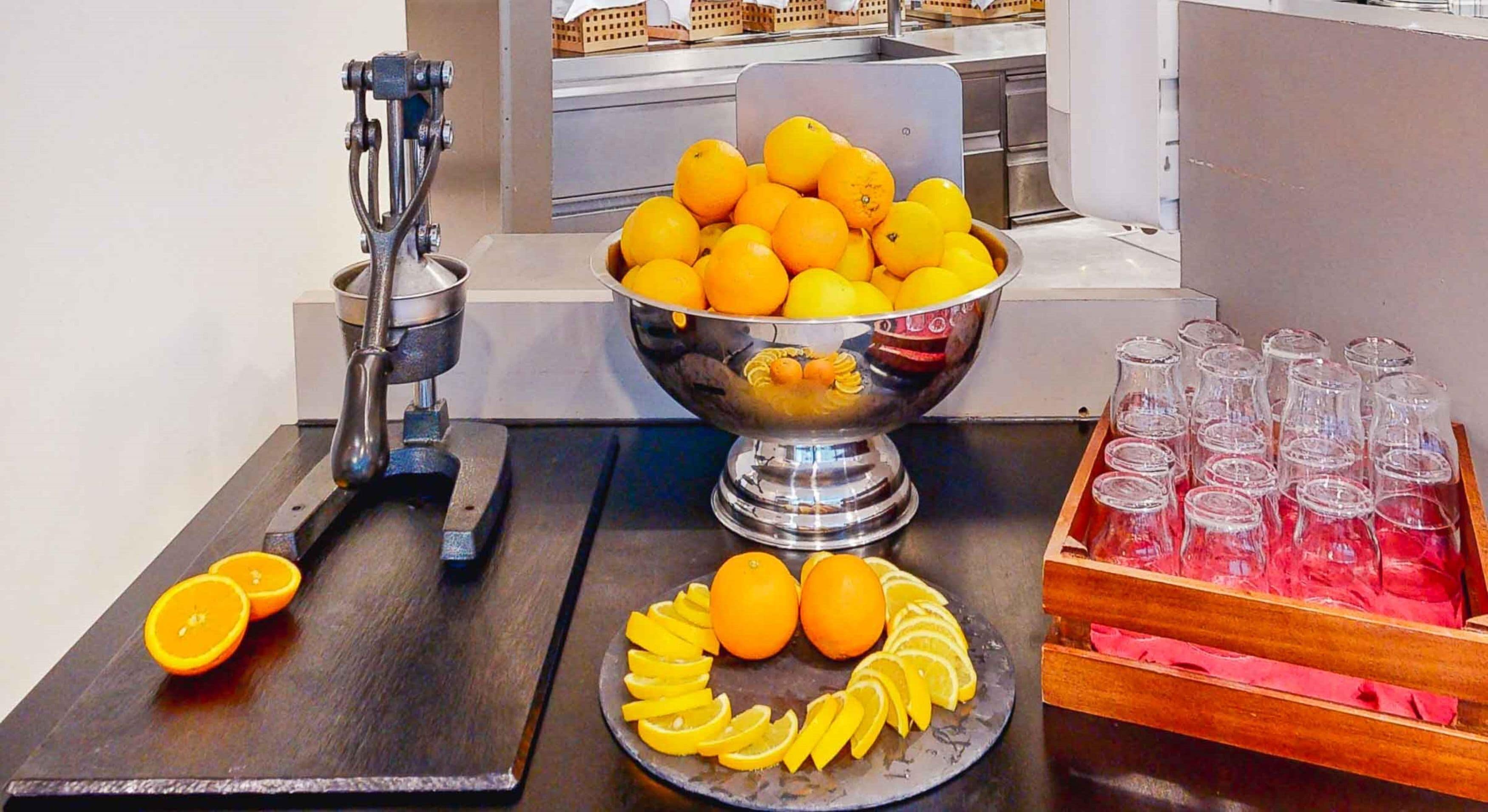 Ett buffébord med en skål med apelsiner, en citruspress och ett fat med skivade apelsiner.