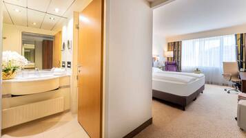A hotel room with a large bed, a desk, and a bathroom with a vanity and mirror.