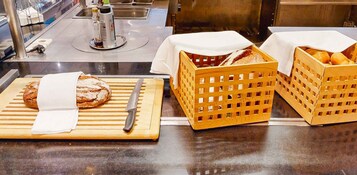 A kitchen counter with a loaf of bread on a cutting board, a knife, and two baskets of bread covered with white cloths.