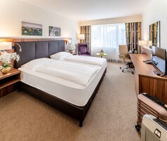 Quarto de hotel com uma cama grande, uma escrivaninha com computador, uma cadeira e uma pequena mesa com uma tigela de frutas.