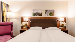 A hotel room with a double bed, two nightstands with lamps, a wooden headboard, and two wall-mounted pictures. - PLAZA Premium Wien (Vienna)
