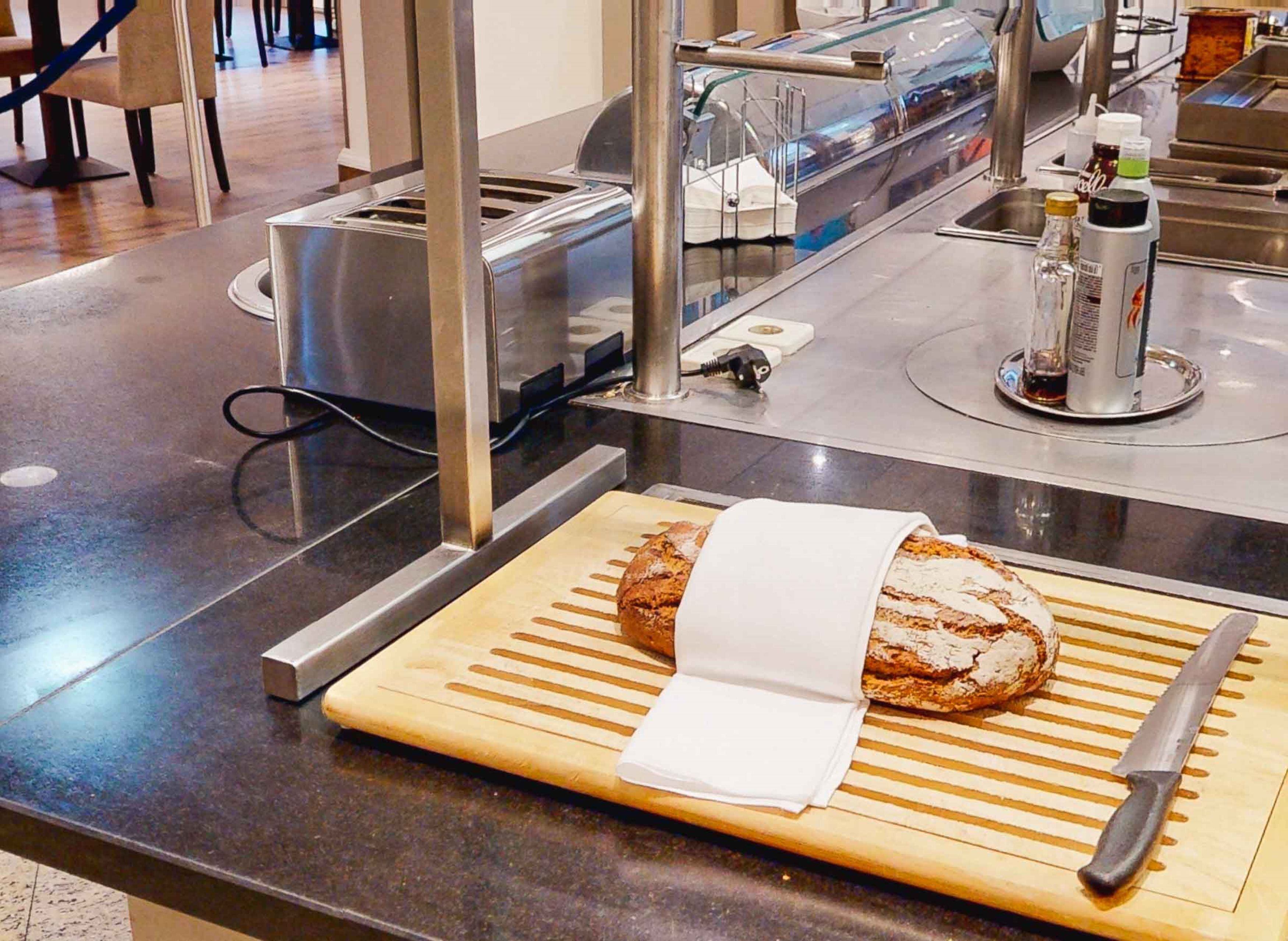 A bakery display with a loaf of bread on a wooden board, a knife, and a soda bottle.