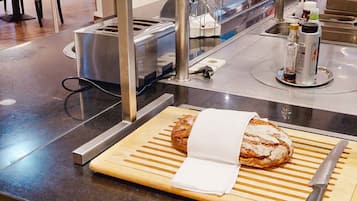 Mostra de forn amb una barra de pa sobre una taula de fusta, un ganivet i una ampolla de refresc.
